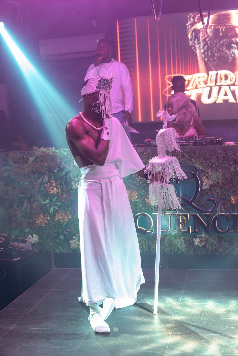 A performer in white with a fringed headdress and staff